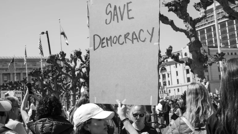 Demonstranci, a wśród nich kodbieta trzymająca transparent z napisem "SAVE DEMOCRACY".